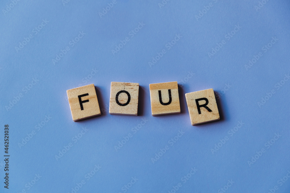 Number four laid out from tiles in words. Wooden tiles on a blue background with letters. View from above. Copy space. Number four laid out from tiles in words. Wooden tiles on a blue background with letters. View from above. Copy space.