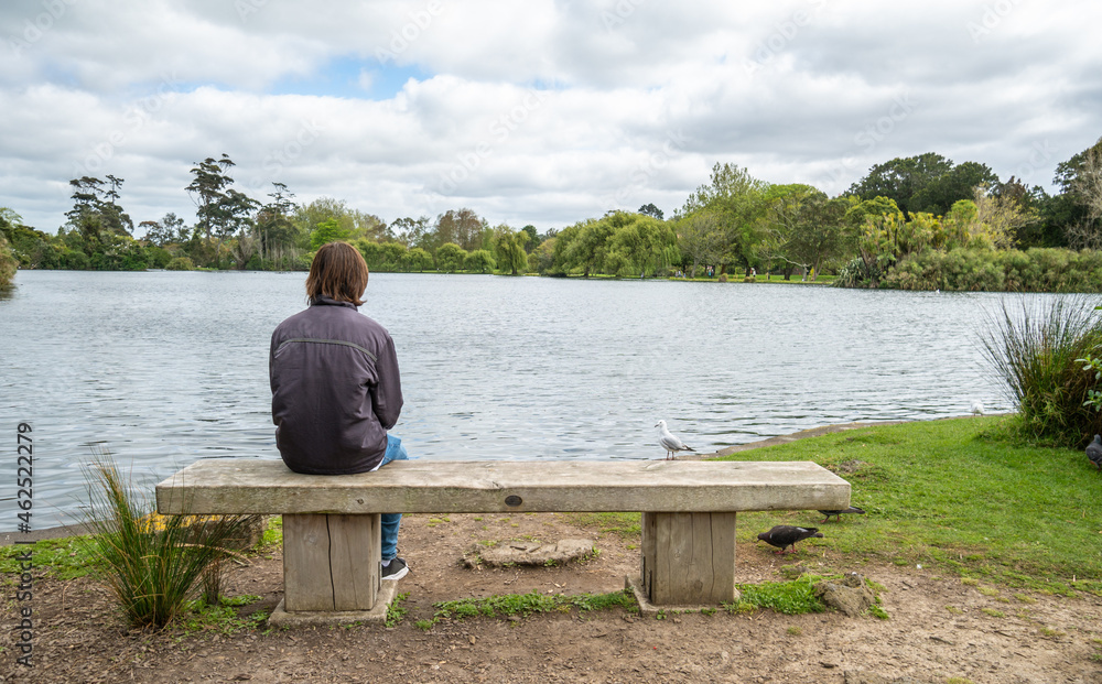 Teenage Boy Sitting on Park Bench in Front of Lake in Auckland New Zealand - with copy space Teenage Boy Sitting on Park Bench in Front of Lake in Auckland New Zealand - with copy space