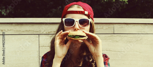 close up face of funny young woman eating a burger fast food in the city