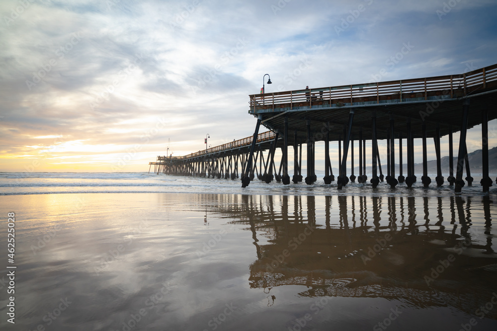 Pismo Beach pier at sunset with beautiful sun reflections on sandy beach, and beautiful cloudy sky on background, California central Coast