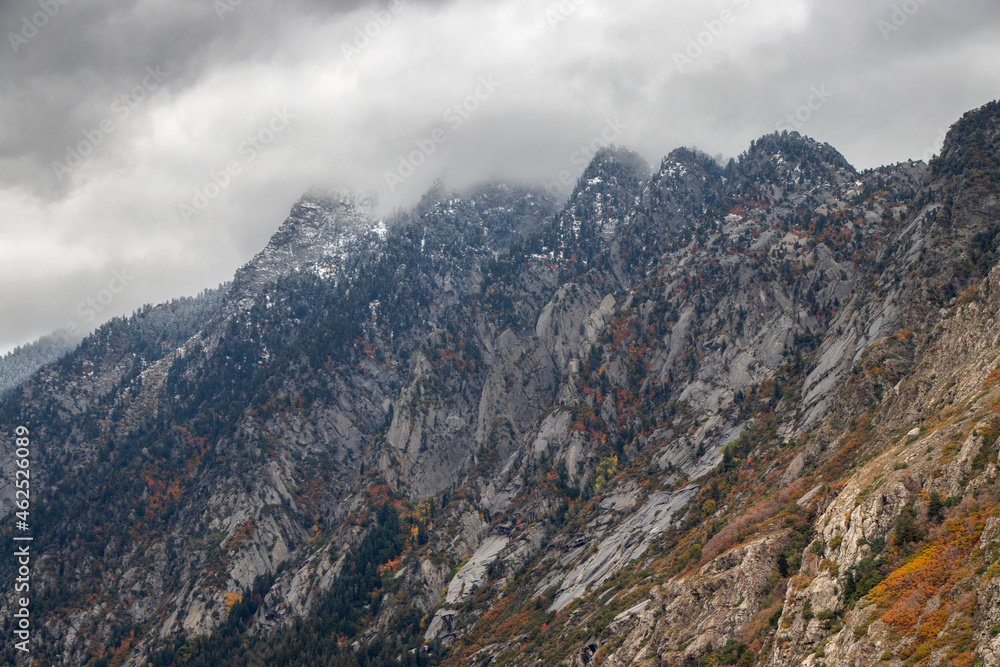 Granite mountains ascending into the clouds in Little Cottonwood Canyon, Utah during Autumn