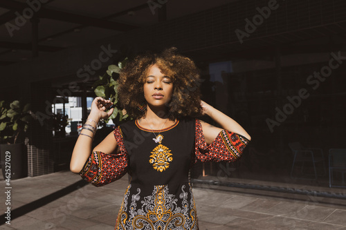 Beautiful African American woman wearing a casual black and red dress tiding up her afro hair with eyes shut introspective.