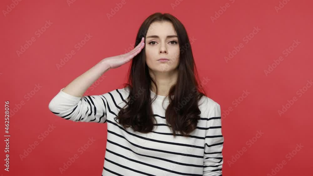 Yes, sir. Portrait of serious woman saluting commander, listening order with obedient expression, wearing casual style long sleeve shirt. Indoor studio shot isolated on red background. Yes, sir. Portrait of serious woman saluting commander, listening order with obedient expression, wearing casual style long sleeve shirt. Indoor studio shot isolated on red background.