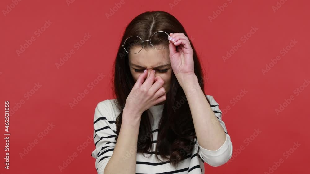 Portrait of exhausted woman takes off glasses, feels eyes pain, being tired from long hours working, wearing casual style long sleeve shirt. Indoor studio shot isolated on red background. Portrait of exhausted woman takes off glasses, feels eyes pain, being tired from long hours working, wearing casual style long sleeve shirt. Indoor studio shot isolated on red background.