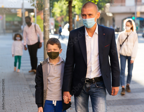 Father with son in protective face mask for spreading of virus disease prevention walking on city street. High quality photo