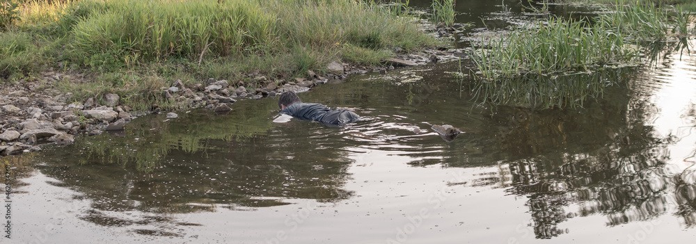 the body of a man who drowned lies face down in the water, the lifeless body of a murdered young man on the river at low tide at sunset the body of a man who drowned lies face down in the water, the lifeless body of a murdered young man on the river at low tide at sunset