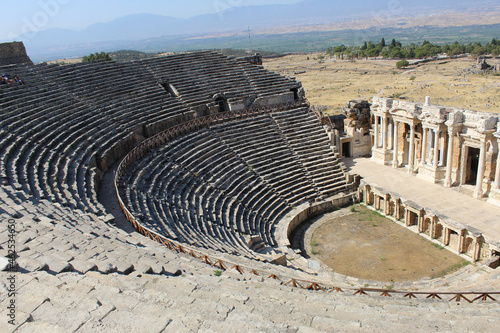 the ancient stone amphitheater and the remains of columns and portico are viewed from above