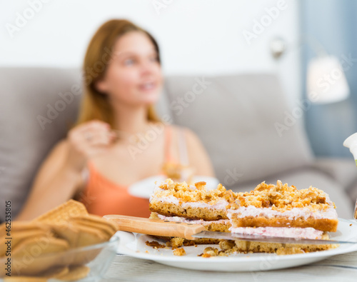 Positive woman sitting on sofa with plate with fresh cake