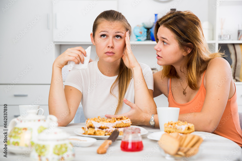 Female talking with young sad friend at the table with cake at home