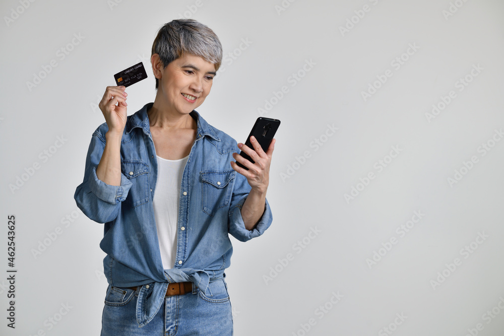 Fototapeta premium Portrait of middle aged Asian woman 50s wearing casual denim shirt white t-shirt holding smartphone and credit card shopping online isolated on white background