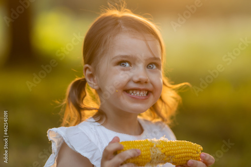 Young funny girl eating a boiled corn. Child in the garden  girl eating corn on the cob  GMO free food. Kids eat fruit outdoors. Healthy snack for children. summer concept. High quality photo