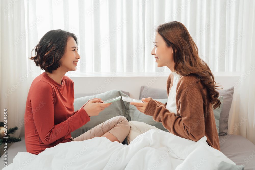 Smiling Two Asian young lovely couple repose on white bed and happy playing with smartphone and social media. Smiling Two Asian young lovely couple repose on white bed and happy playing with smartphone and social media.