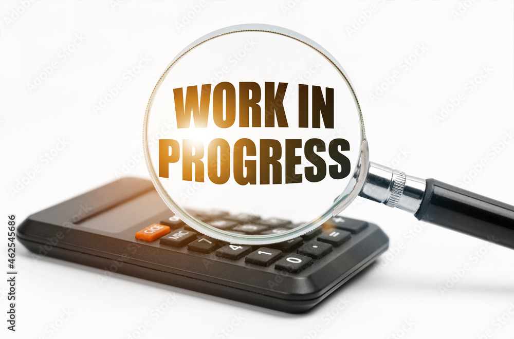 On the table is a calculator and a magnifying glass, inside which the inscription - Work in Progress On the table is a calculator and a magnifying glass, inside which the inscription - Work in Progress