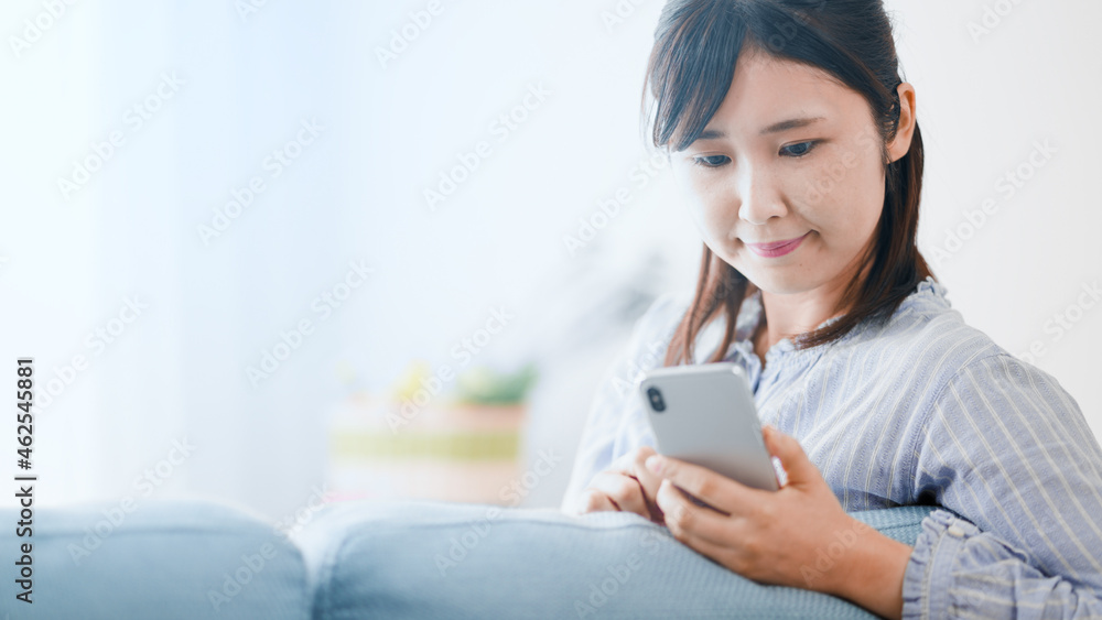 ソファーに寄りかかりながらスマートフォンを使う女性 ソファーに寄りかかりながらスマートフォンを使う女性
