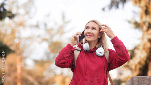 Using mobile outdoor. Attractive happy woman talking on a cellphone in an autumn urban park, selective focus, format photo 16x9