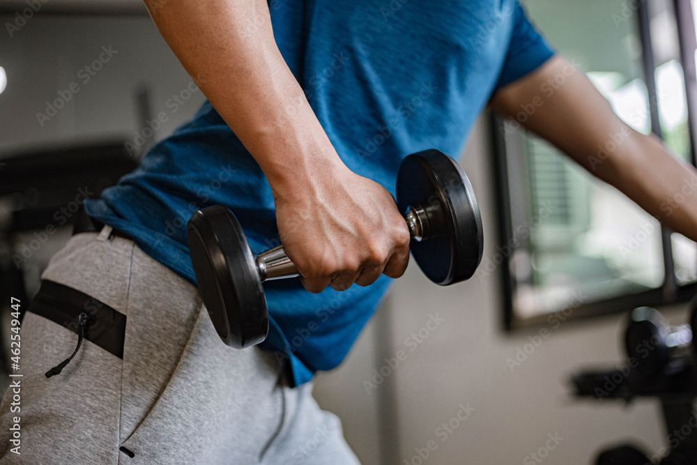Training gym concept a young adult using his muscular strong arm lifting a dumbbell upward and downward in the gym Training gym concept a young adult using his muscular strong arm lifting a dumbbell upward and downward in the gym