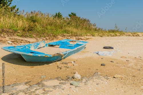 Damaged flat bottom boat filled with sand abandoned on beach.