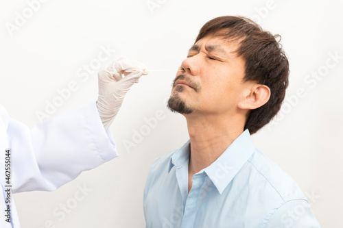 Covid diagnostic procedure. Doctor making nasal PCR test for adult asian man  using sterile swab stick  Coronavirus COVID-19 ATK diagnostic.