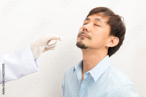 Covid diagnostic procedure. Doctor making nasal PCR test for adult asian man, using sterile swab stick, Coronavirus COVID-19 ATK diagnostic.