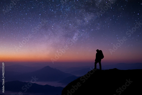 A young tourist with a bag is standing looking at the stars. The Milky Way and the beauty of the night sky alone on the top of the mountain. He felt successful at reaching his intended destination.