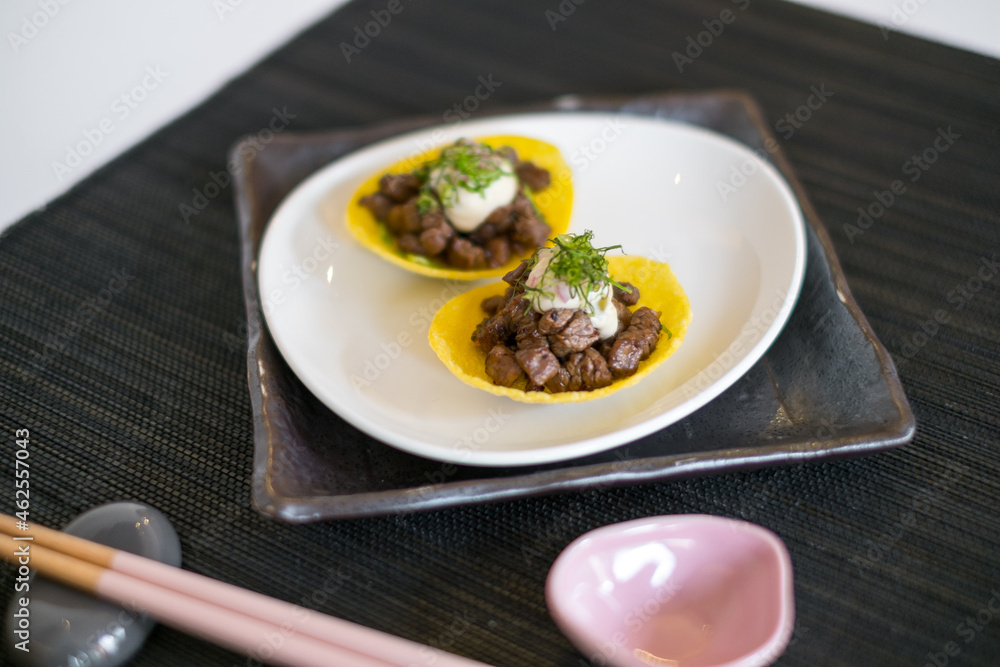 Asian style meat tartlets on white plate with wooden chopsticks on black mat in Japanese restaurant. close up, photo for the menu