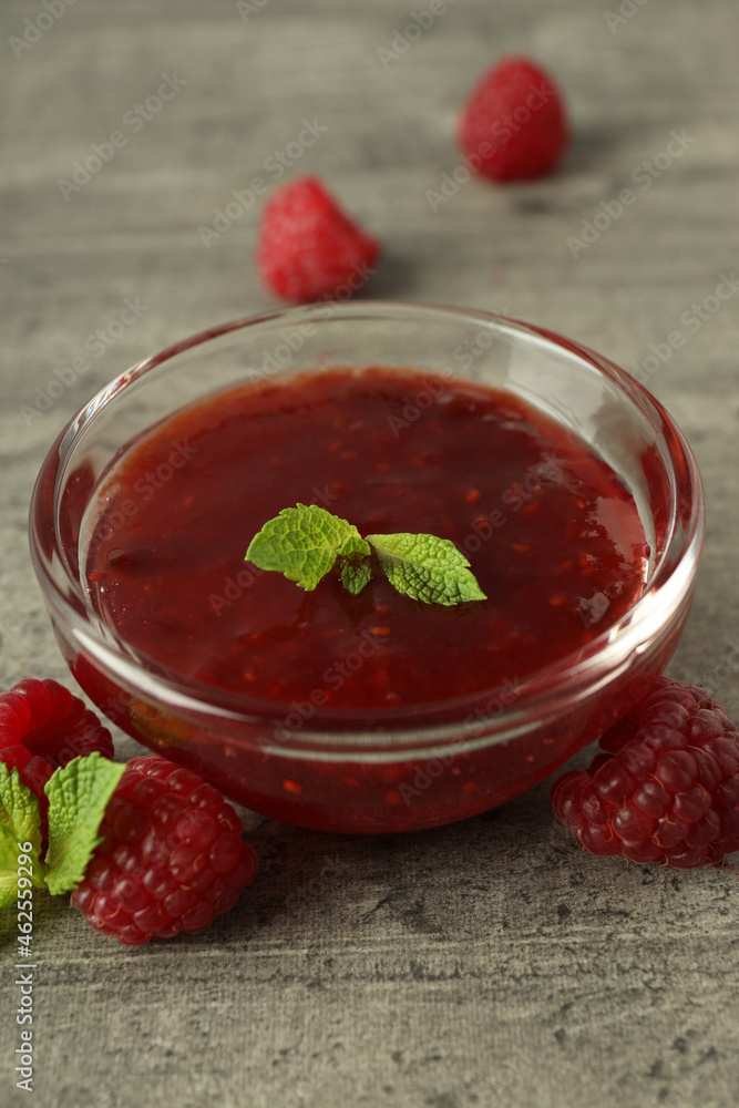 Glass bowl of raspberry jam with ingredients on gray textured background Glass bowl of raspberry jam with ingredients on gray textured background