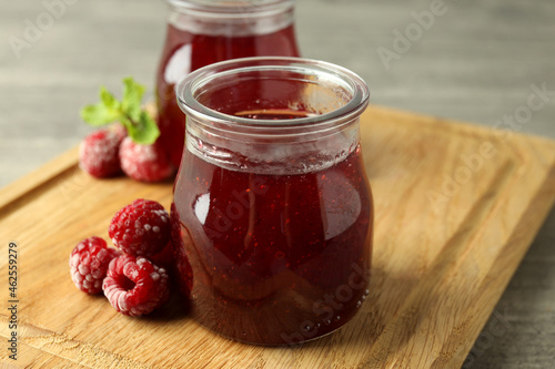 Glass jars of raspberry jam with ingredients on wooden board photo