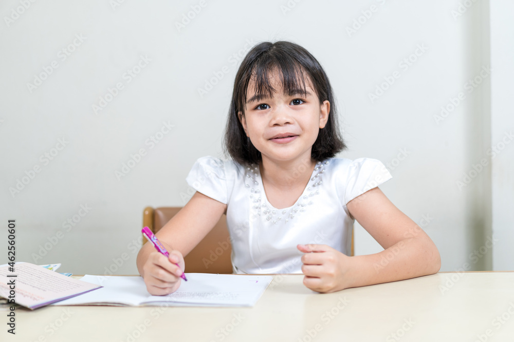Cheerful Asian little girl children student writing on notebook doing homework and self study at home. Education Homeschool Concept Stock Photo Cheerful Asian little girl children student writing on notebook doing homework and self study at home. Education Homeschool Concept Stock Photo