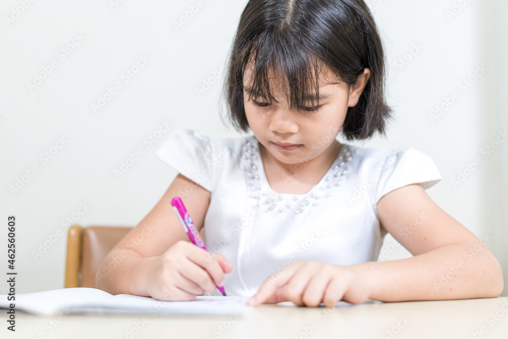 Cheerful Asian little girl children student writing on notebook doing homework and self study at home. Education Homeschool Concept Stock Photo Cheerful Asian little girl children student writing on notebook doing homework and self study at home. Education Homeschool Concept Stock Photo
