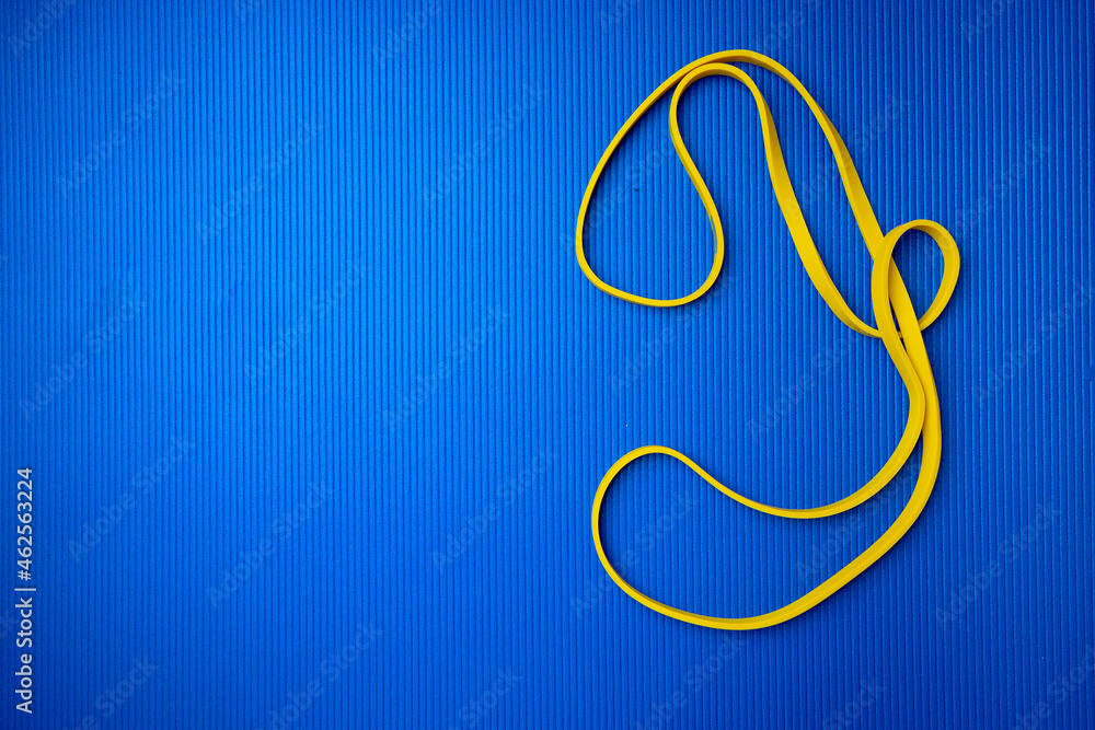 Obraz premium Yellow fitness rope on blue mat background