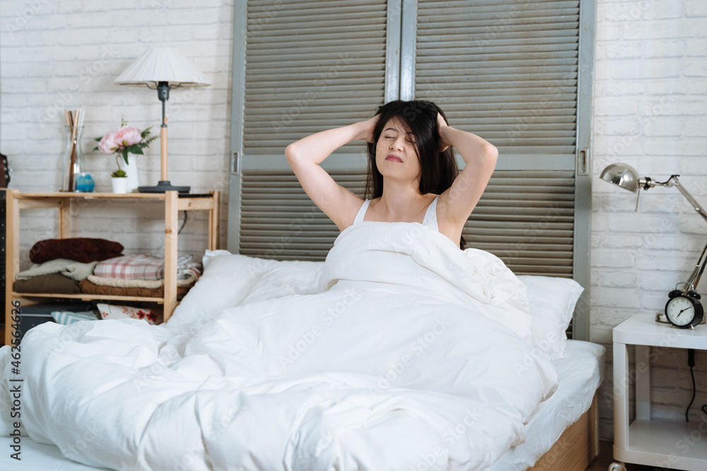 Unhappy young woman waking up in bed feeling ache in head