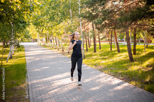 A girl in a black sports uniform is jogging in the evening park. Self-sports concept. © Михаил Гута
