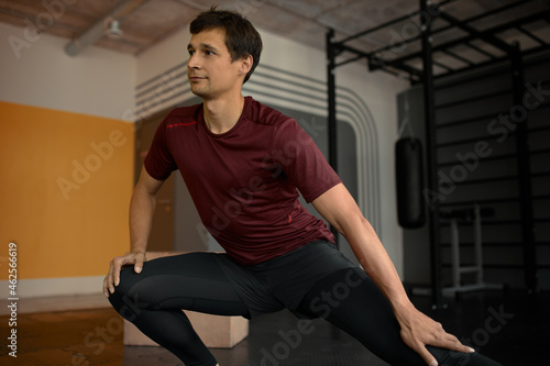 Portrait of young attractive fitness trainer showing stretching exercises in trendy sportswear isolated on gym surroundings of sports equipment for different purpose. Body and shape concept
