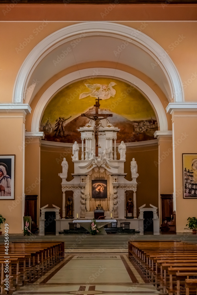 Fototapeta premium Shkoder, Albania - June 21, 2021: Interior of St. Stephen's Catholic Church in Shkoder, vertical. Temple hall with wooden benches against the background of the altar with a crucifix