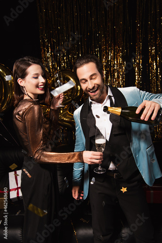 Photography happy man pouring champagne near elegant woman during new year party on black