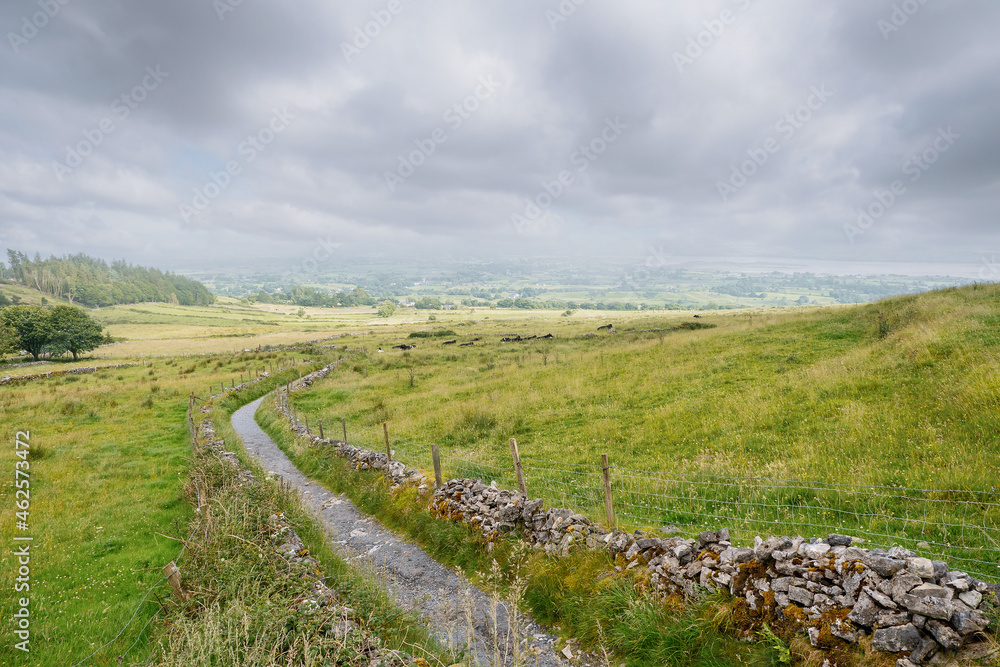 Small walking path with great view on beautiful country side with green fields separated by stone fence. Irish country side. County Sligo, Ireland. Small walking path with great view on beautiful country side with green fields separated by stone fence. Irish country side. County Sligo, Ireland.