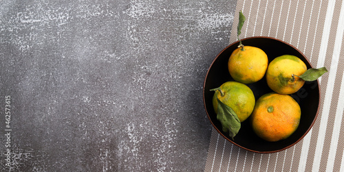 Tangerines with leaves in a bowl on a dark background. Top view  flat lay