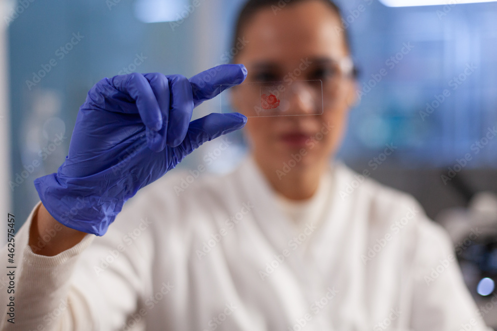 Naklejka premium Chemist doctor holding medical slice analyzing blood sample while working at biochemistry experiment in pharmaceutical hospital laboratory. Microbiologist woman developing vaccine against covid19