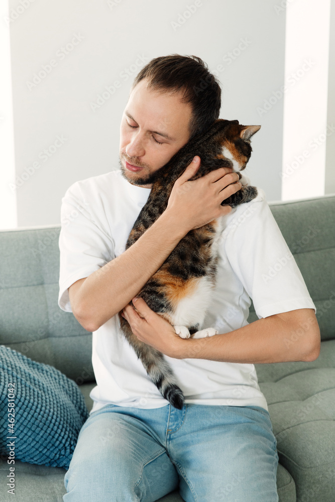 Upset man hugging beloved cat. Tired unhappy millennial male cuddling with cute pet sit on couch at home. Depressed guy bonding with animal friend. Stress relief, friendship and togetherness concept Upset man hugging beloved cat. Tired unhappy millennial male cuddling with cute pet sit on couch at home. Depressed guy bonding with animal friend. Stress relief, friendship and togetherness concept