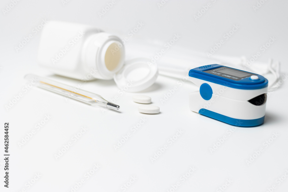 Portable pulse oximeter, thermometer and pills on white background