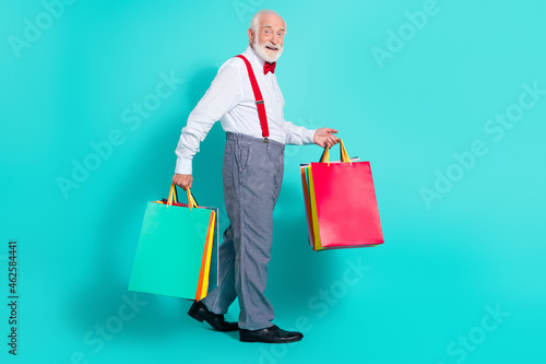 Full length body size view of attractive cheerful grey-haired man carrying new things isolated over bright teal turquoise color background