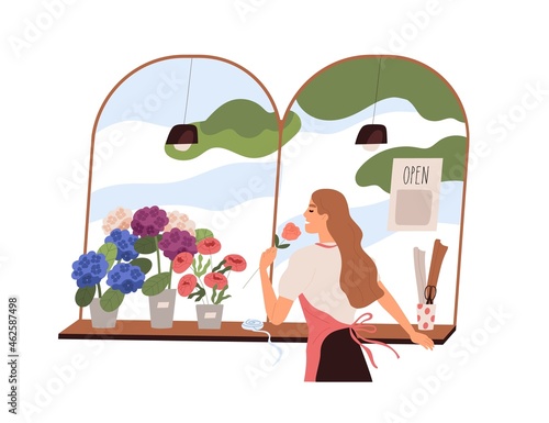 Florist woman smelling fresh flower at flora shop. Vendor in retail store wit...