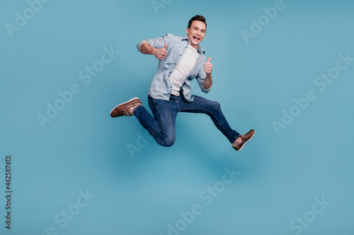 Full size profile side photo of young man jump show fingers thumbs-up select suggest ad isolated over blue color background