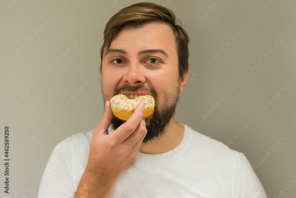Handsome man with a beard bites a donut on a gray background celebrates a birthday Handsome man with a beard bites a donut on a gray background celebrates a birthday