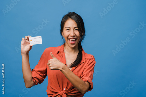 Young Asia lady show credit bank card with positive expression, smiles broadly, dressed in casual clothing feeling happiness and stand isolated on blue background. Facial expression concept. © tirachard