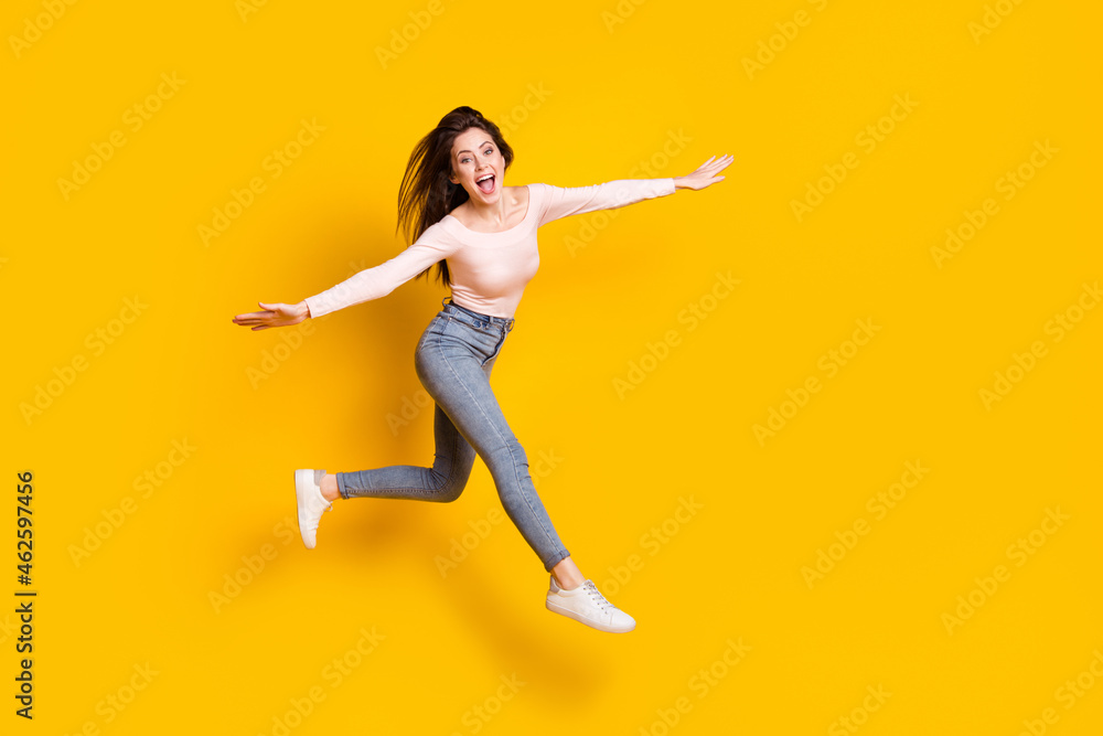 Full size photo of young happy excited smiling girl flying hold hands wings isolated on yellow color background