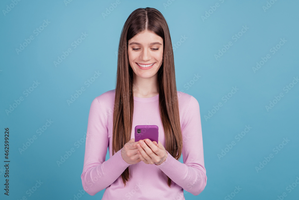 Photo of attractive cheerful girl happy positive smile use smartphone isolated over blue color background Photo of attractive cheerful girl happy positive smile use smartphone isolated over blue color background