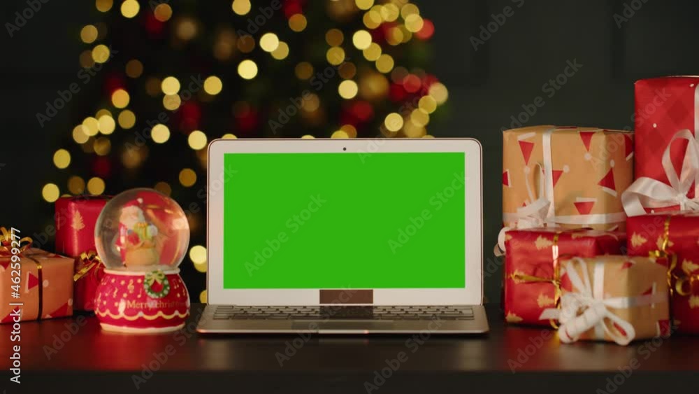 Laptop with green screen on table with Christmas decorations against Christmas tree Laptop with green screen on table with Christmas decorations against Christmas tree