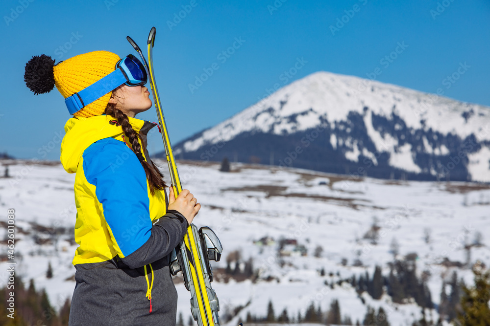 young smiling pretty woman holding ski. mountains on background