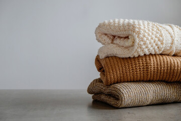 Bunch of knitted warm pastel color sweaters with different knitting patterns folded in stack, clearly visible texture. Stylish fall-winter season knitwear clothing. Close up, copy space for text.